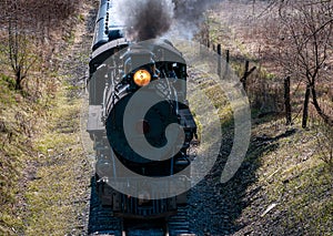 Industrial locomotive in motion, emitting a white plume of steam from its smokestack