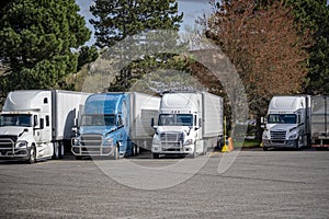 Industrial long haul big rigs semi trucks with loaded semi trailers standing in row on the truck stop parking lot for truck