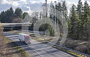 Industrial long haul red big rig semi truck with dry van semi trailer running on the turning divided highway road with bridge