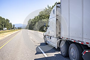 Industrial long hauler big rig semi truck transporting cargo in dry van semi trailer running on the straight wide highway road