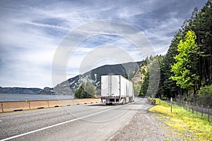 Big rig white semi truck tractor transporting commercial cargo in dry van semi trailer running on the winding road along the river