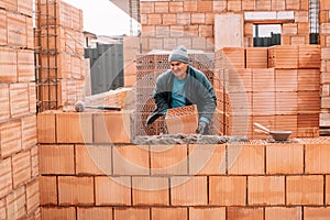 Industrial male bricklayer installing bricks on construction site