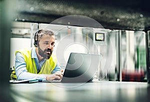 An industrial man engineer with headset and laptop in a factory, working.