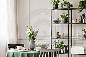 Industrial metal shelf with dishes and plants in bright dining room with round table with chairs