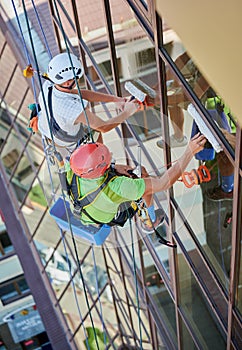 Industrial mountaineering worker cleaning window outside building.