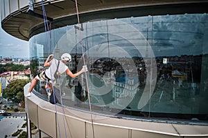 Industrial mountaineering worker cleaning window outside building.