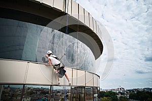 Industrial mountaineering worker cleaning window outside building.