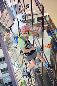 Industrial mountaineering worker cleaning window outside building.