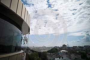 Industrial mountaineering worker cleaning window outside building.