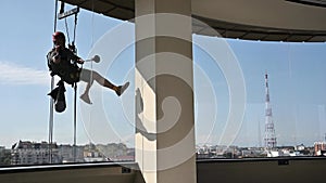 Industrial mountaineering worker washing glass windows of high-rise building