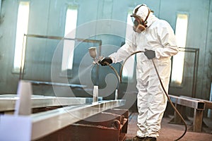 industrial painter in chamber spraying paint on metal detail