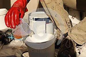 Industrial painter using red chemical safety protection glove while pouring harder from measuring cup back into paint bucket