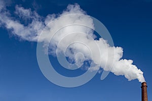 The industrial pipe produces white smoke in the blue sky. Concept Love Nature, Ecology and Technological Progress. Copy space.