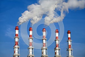 Industrial pipes with white smoke over blue sky. Horizontal photo