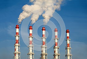 Industrial pipes with white smoke over blue sky. Horizontal photo