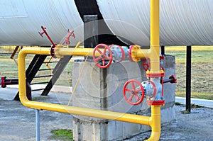 Industrial piping with steel flanges and bolts on oil field. Fuel pipes valves and crude pipelines. Gas drilling derricks at