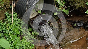 Industrial polluted waste water flowing from a black sewer pipe into a river in close up