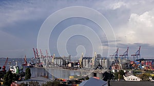 Industrial port landscape with cargo cranes and grain elevators under cloudscape. 4K panning