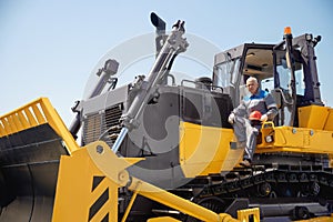 Industrial portrait of working man, excavator driver climbs into cab to perform work on construction site