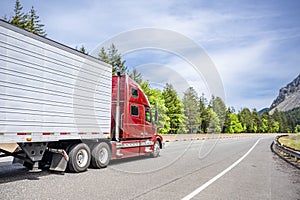 Industrial pro red big rig semi truck transporting cargo in reefer semi trailer driving on the divided highway road in Columbia