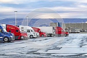 Industrial professional big rigs semi trucks with loaded semi trailers standing on the truck stop parking lot for truck drivers