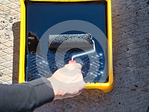 Industrial repair and painting. Painter's hand with paint roller over tray of black paint. Background