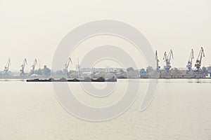 Industrial river waterscape with dry cargo barge and cargo terminal in morning fog