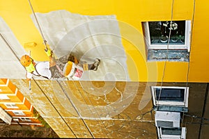 Industrial rope access worker hanging from the building while painting the exterior facade wall. Industrial alpinism concept image