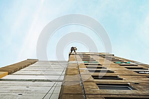 Industrial rope access worker hanging from the building while painting the exterior facade wall. Industrial alpinism concept image