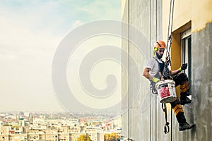 Industrial rope access worker hanging from the building while painting the exterior facade wall. Industrial alpinism concept image