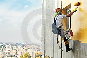 Industrial rope access worker hanging from the building while painting the exterior facade wall. Industrial alpinism concept image