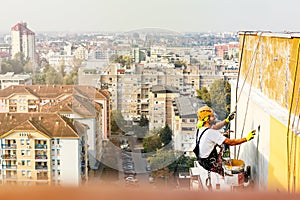 Industrial rope access worker hanging from the building while painting the exterior facade wall. Industrial alpinism concept image