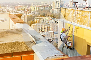 Industrial rope access worker hanging from the building while painting the exterior facade wall. Industrial alpinism concept image