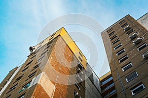 Industrial rope access worker hanging from the building while painting the exterior facade wall. Industrial alpinism concept image