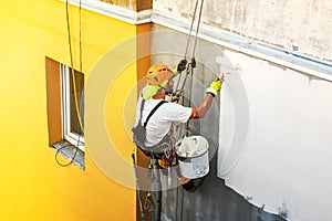 Industrial rope access worker hanging from the building while painting the exterior facade wall. Industrial alpinism concept image