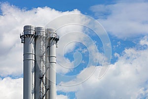 Industrial round smoke-free pipes with an observation deck and a staircase against a clear blue sky with white clouds