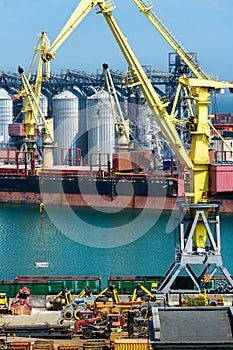 Industrial seaport infrastructure, sea, cranes and dry cargo ship, grain silo, bulk carrier vessel and grain storage elevators,