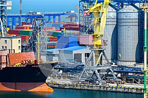 Industrial seaport infrastructure, sea, cranes and dry cargo ship, grain silo, bulk carrier vessel and grain storage elevators,