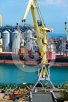 Industrial seaport infrastructure, sea, cranes and dry cargo ship, grain silo, bulk carrier vessel and grain storage elevators,