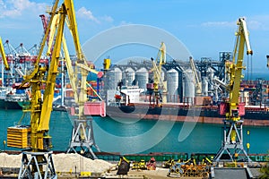 Industrial seaport infrastructure, sea, cranes and dry cargo ship, grain silo, bulk carrier vessel and grain storage elevators,