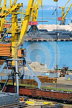 Industrial seaport infrastructure - sea, cranes and metal workpieces, bundles of wire, railcars on railroad, concept of marine
