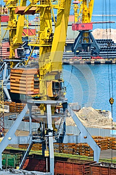Industrial seaport infrastructure - sea, cranes and metal workpieces, bundles of wire, railcars on railroad, concept of marine