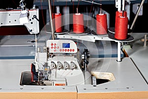 Industrial sewing machine with red spools of thread on a dark workshop background