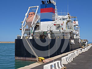 Industrial Ship Moored in Port and a Small Tugboat in the Background