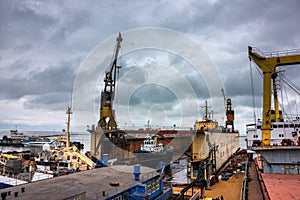 Industrial ship repair yard with floating dock, vessels undergo maintenance. Tugboats assist in marine operations, heavy