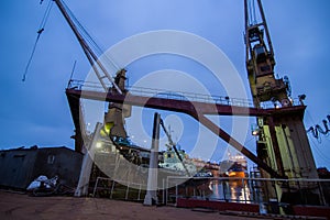 Industrial shipyard at night, floating dock with a ship under repair, lit cranes on duty, marine engineering scene. Ship