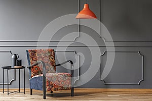 An industrial side table and a boho armchair in an elegant, gray living room interior with molding and place for a coffe table. Re