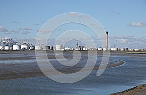 Industrial site with oil storage tanks beneath a blue sky with dark clouds