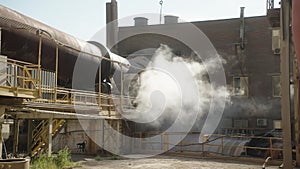 Industrial site with steam release from large pipes and machinery outdoors