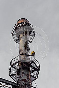 Industrial smokestack with ladders and walkways against a gray sky